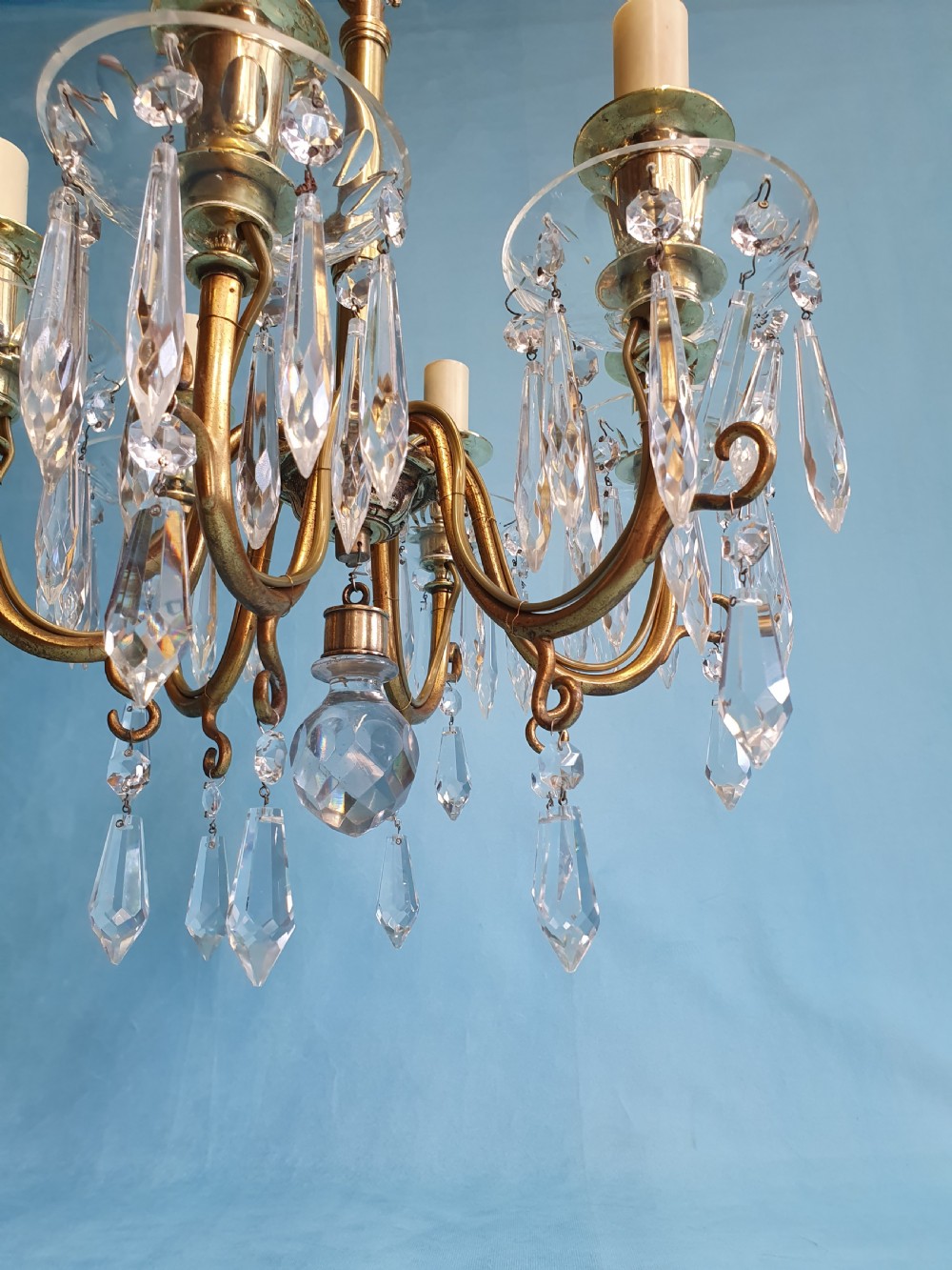 A small six-arm brass chandelier featuring glass drip pans, hanging faceted crystal drops, and a central brass stem with a suspension chain. View VI