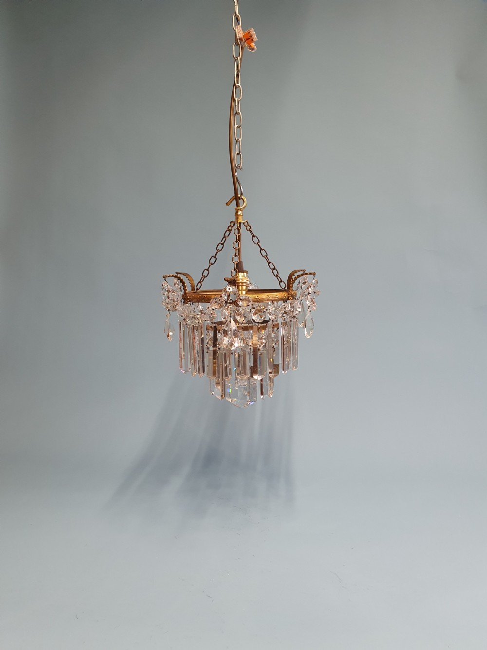 An early 20th-century antique chandelier featuring a circular brass frame decorated with hanging crystal swags and long vertical crystal prisms.