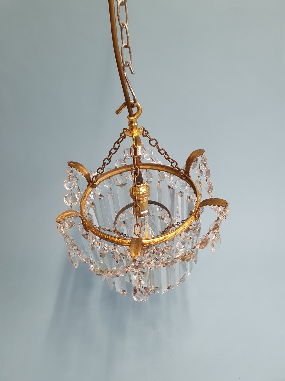 An early 20th-century antique chandelier featuring a circular brass frame decorated with hanging crystal swags and long vertical crystal prisms. View II