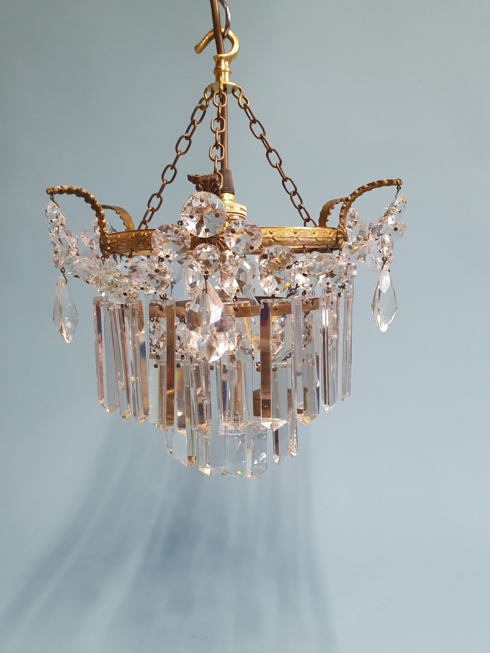 An early 20th-century antique chandelier featuring a circular brass frame decorated with hanging crystal swags and long vertical crystal prisms. View III