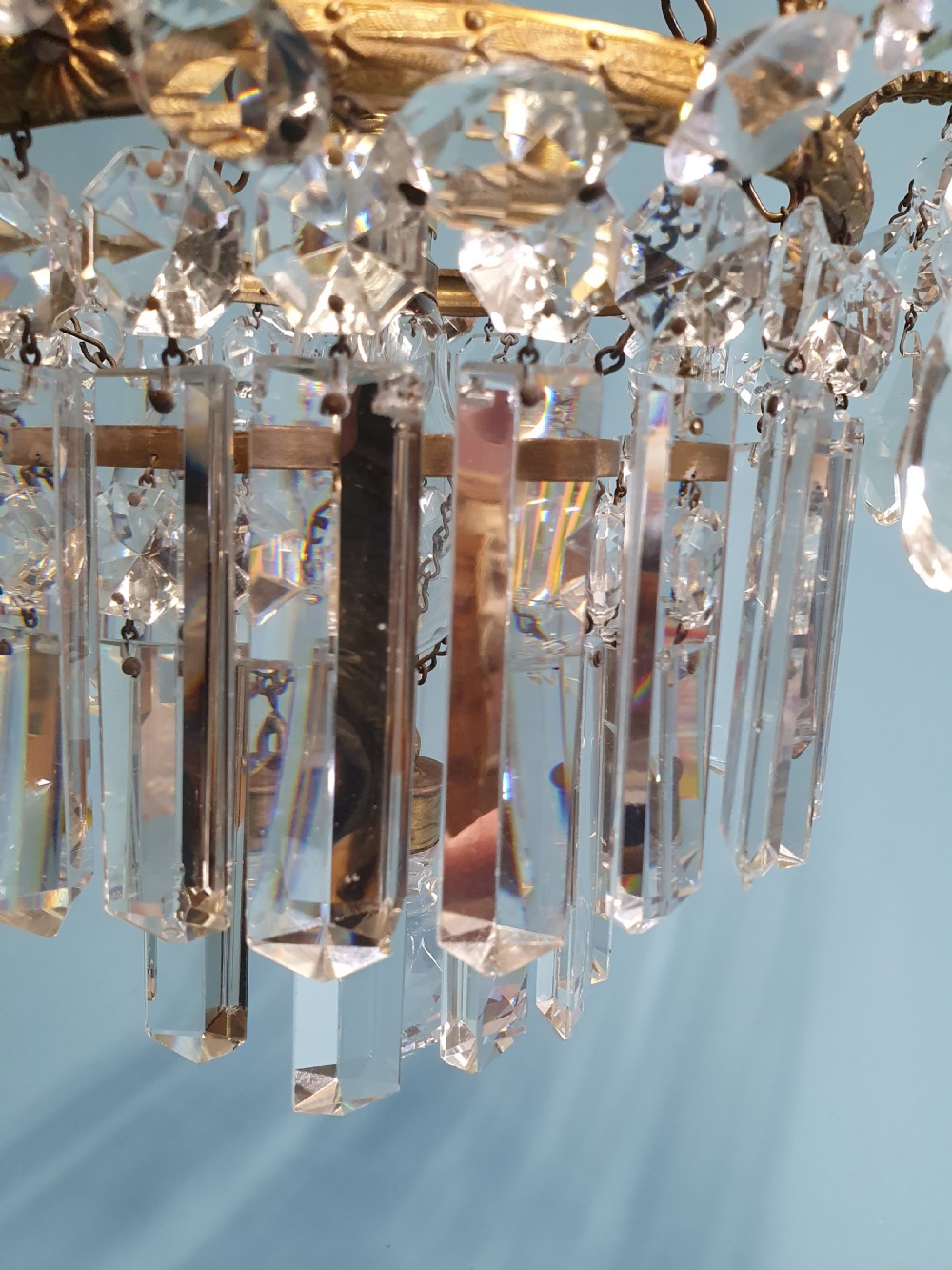 An early 20th-century antique chandelier featuring a circular brass frame decorated with hanging crystal swags and long vertical crystal prisms. View V