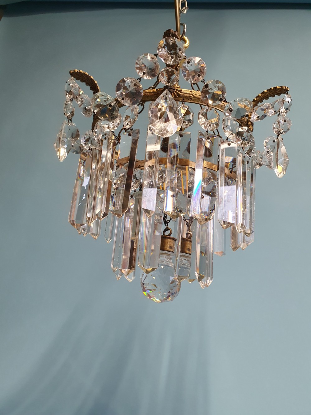 An early 20th-century antique chandelier featuring a circular brass frame decorated with hanging crystal swags and long vertical crystal prisms. View VI