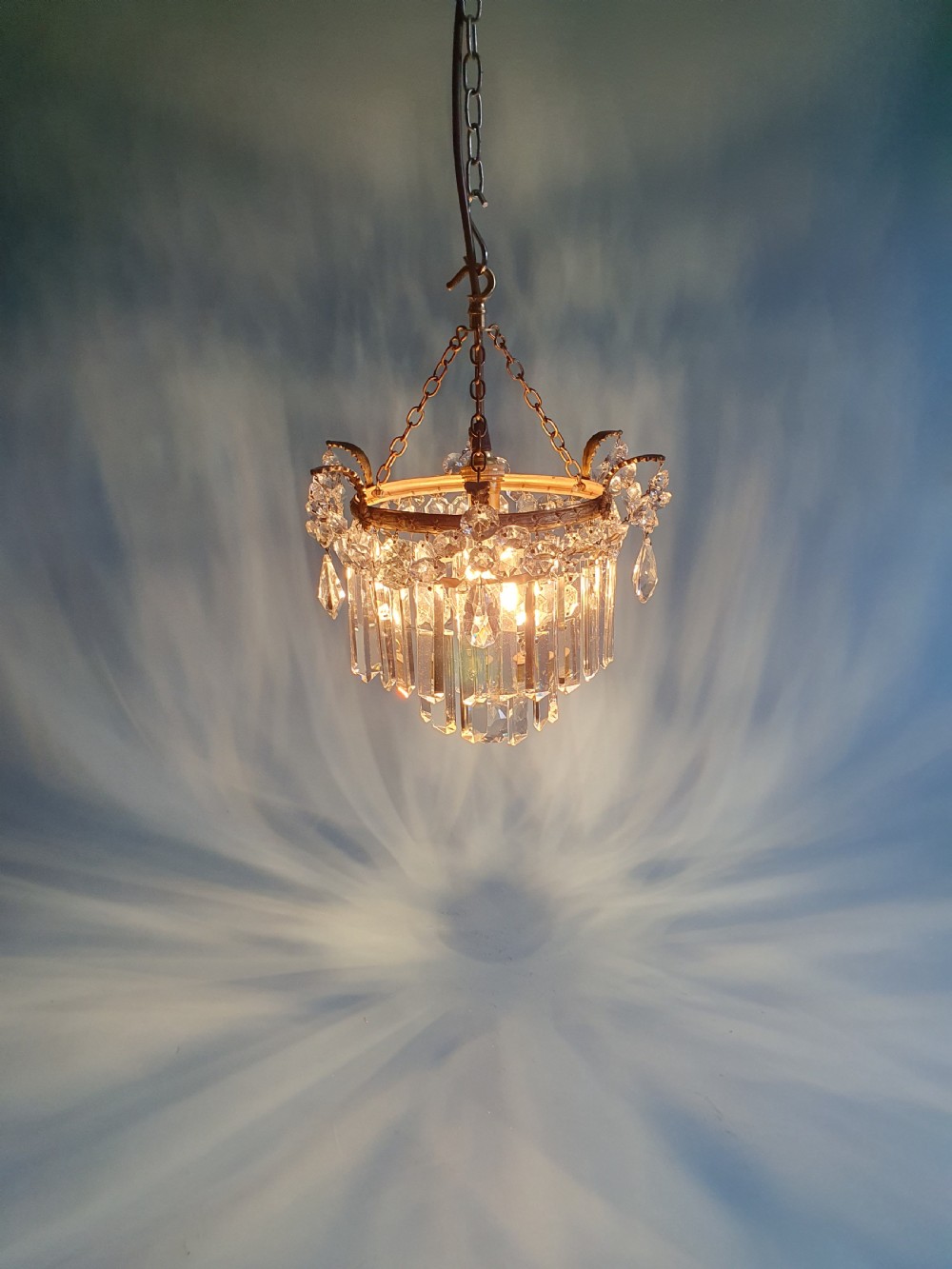 An early 20th-century antique chandelier featuring a circular brass frame decorated with hanging crystal swags and long vertical crystal prisms. View VII