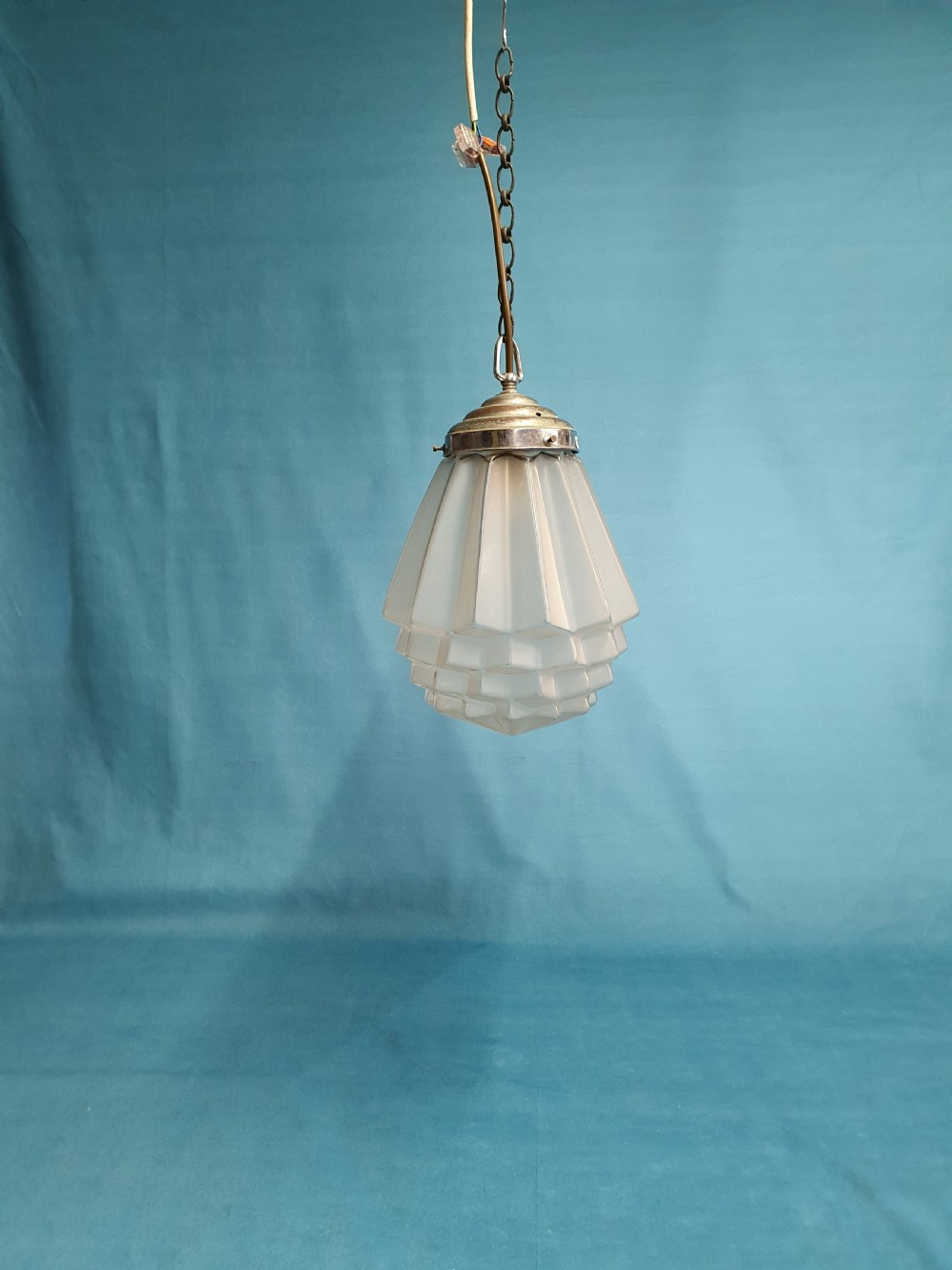 A frosted white Art Deco glass pendant light shade featuring a geometric stepped design suspended by a metal chain.
