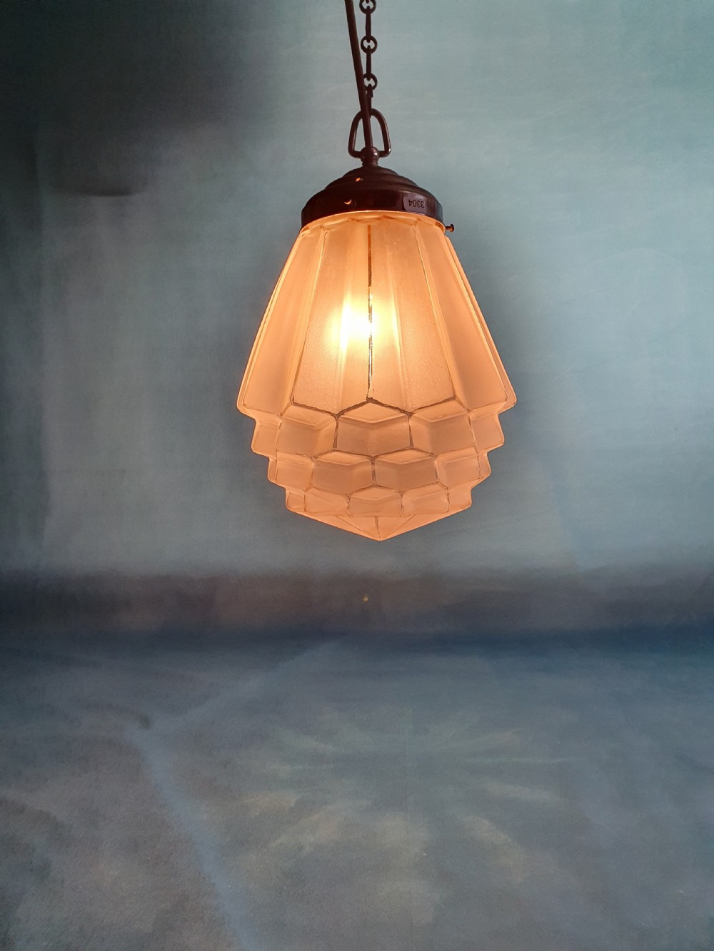 A frosted white Art Deco glass pendant light shade featuring a geometric stepped design suspended by a metal chain. View VII