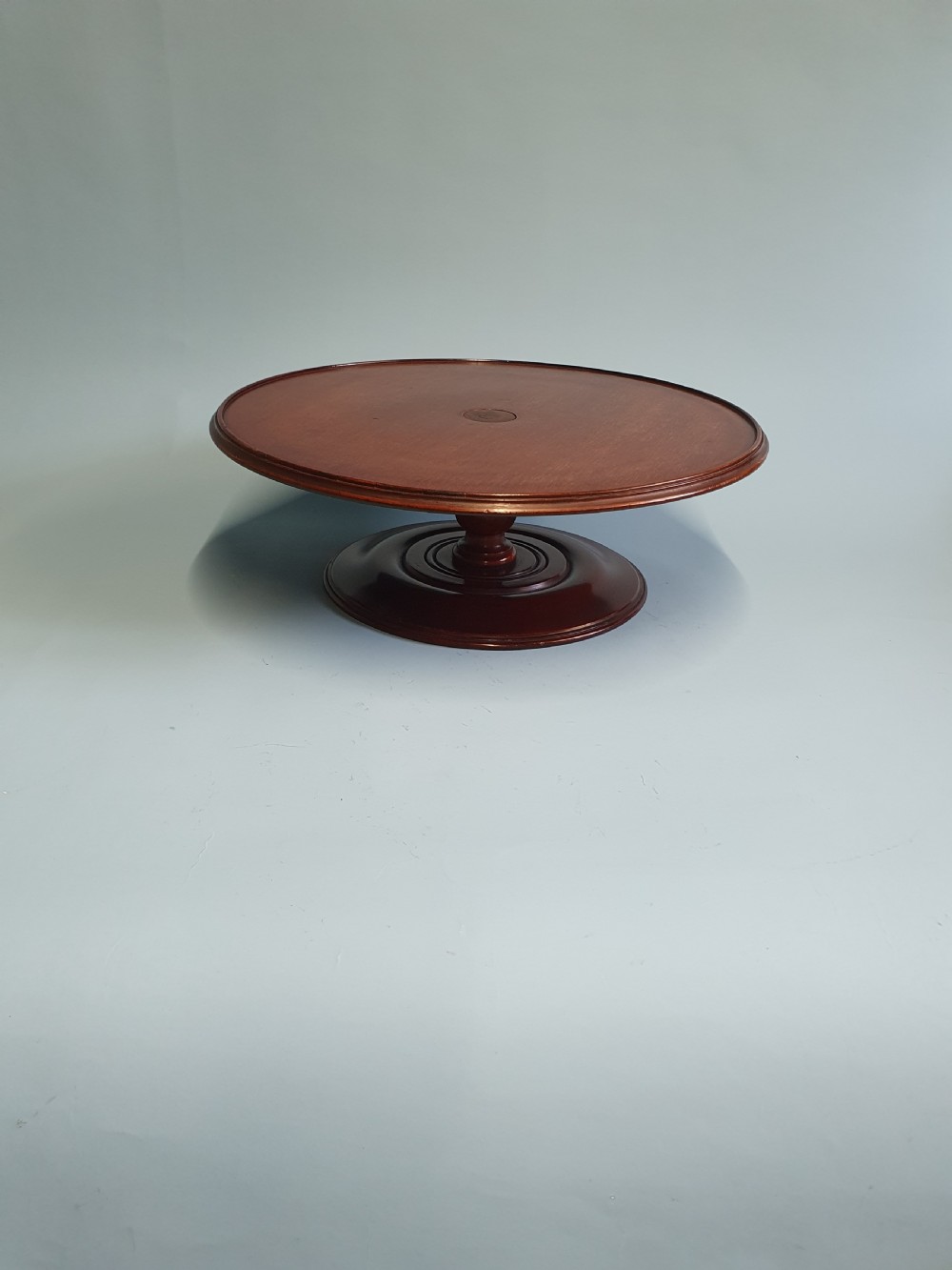 A circular Edwardian mahogany lazy Susan with a raised moulded edge resting on a central turned pedestal base.