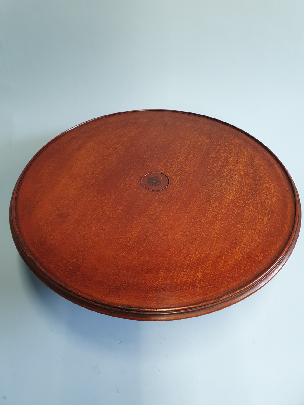 A circular Edwardian mahogany lazy Susan with a raised moulded edge resting on a central turned pedestal base. View II