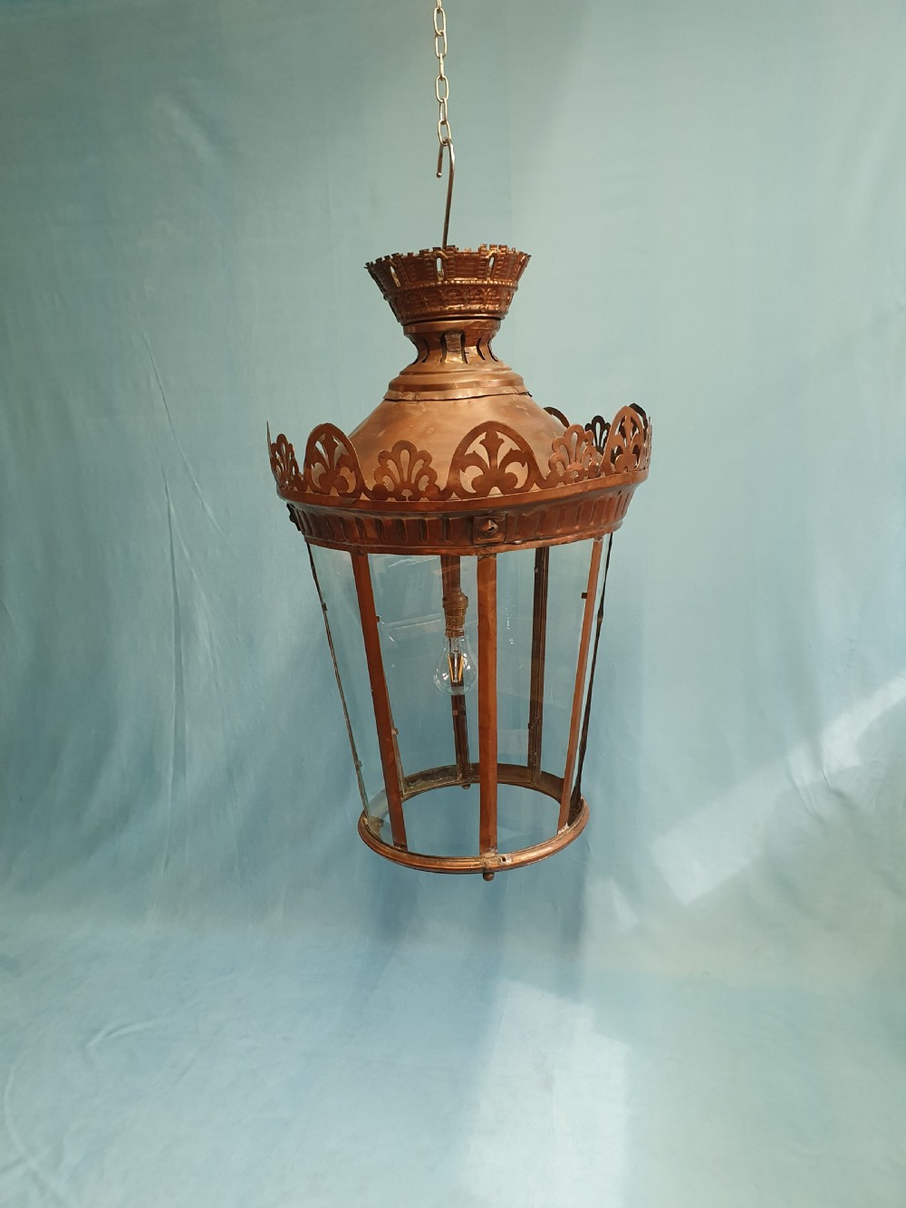 A large circular antique copper lantern with clear glass panels, decorative pierced gallery trim, and suspension chain.