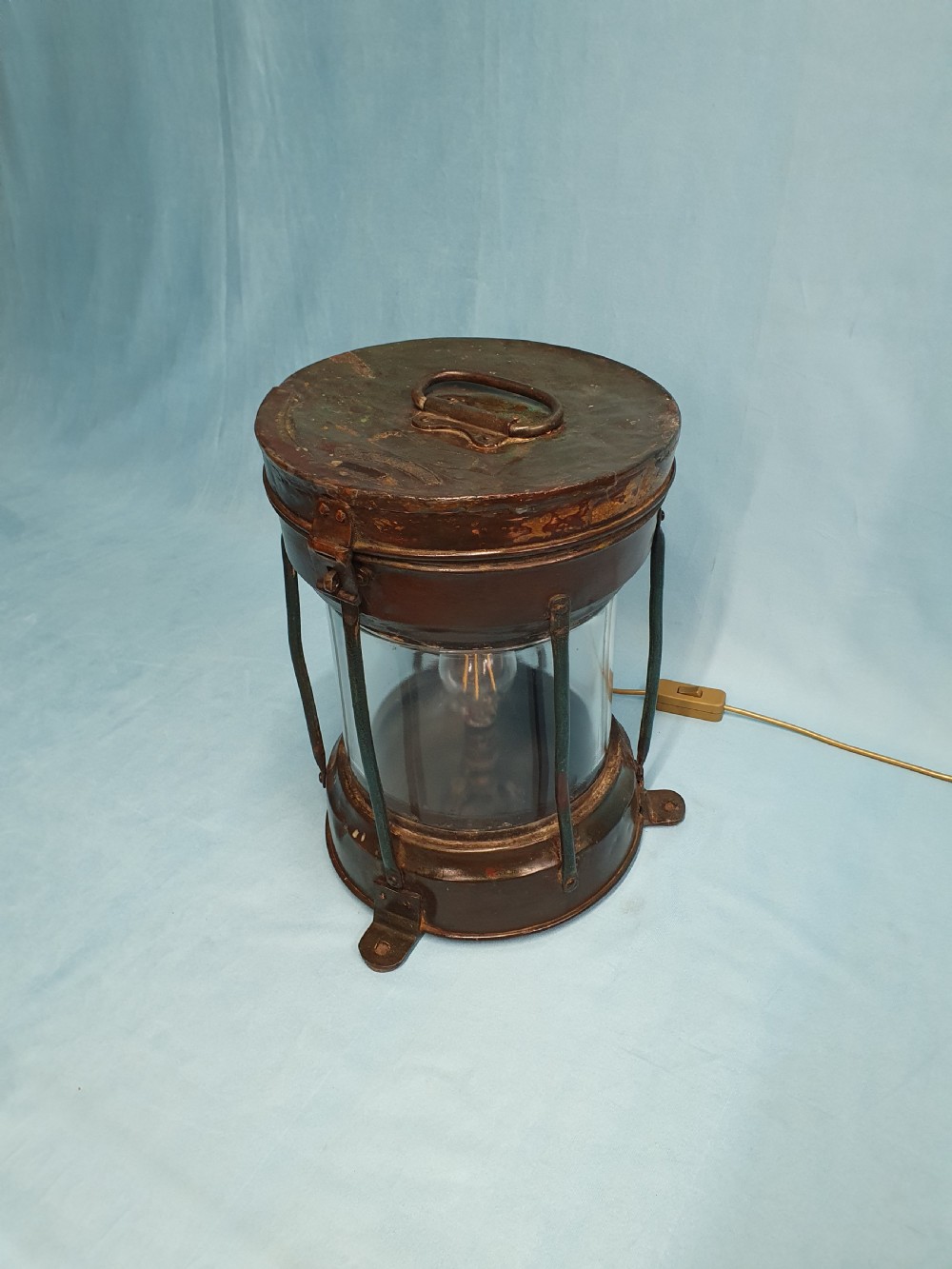 A cylindrical antique copper ship lantern featuring a verdigris patina, clear glass lens, protective metal cage, and top carrying handle. View III