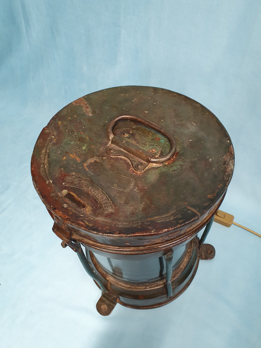 A cylindrical antique copper ship lantern featuring a verdigris patina, clear glass lens, protective metal cage, and top carrying handle. View V