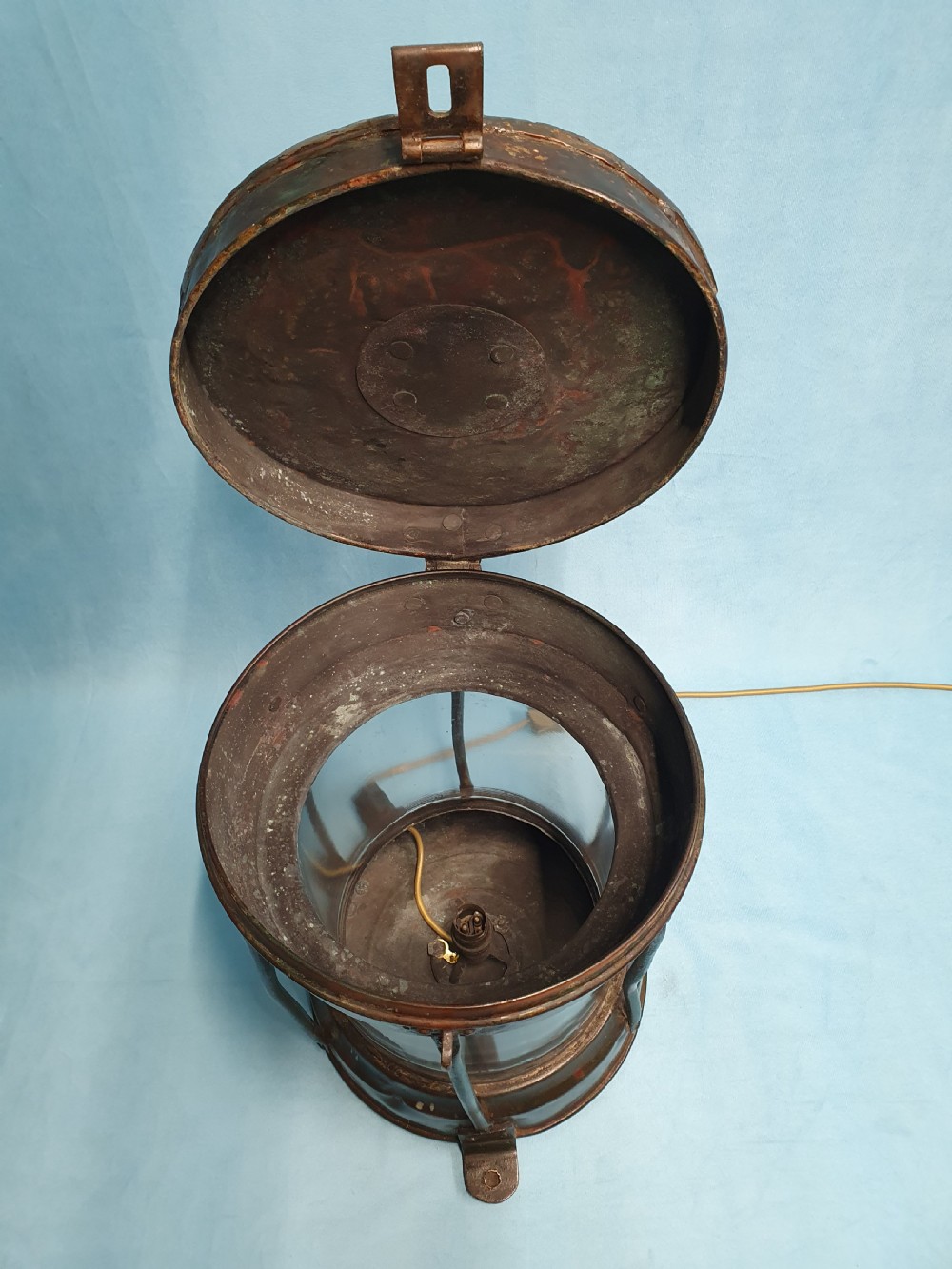 A cylindrical antique copper ship lantern featuring a verdigris patina, clear glass lens, protective metal cage, and top carrying handle. View VI