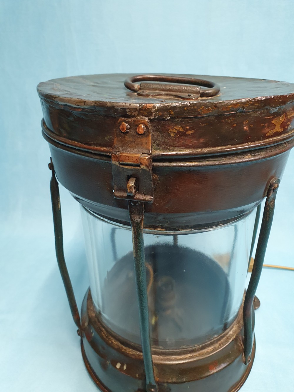 A cylindrical antique copper ship lantern featuring a verdigris patina, clear glass lens, protective metal cage, and top carrying handle. View VII