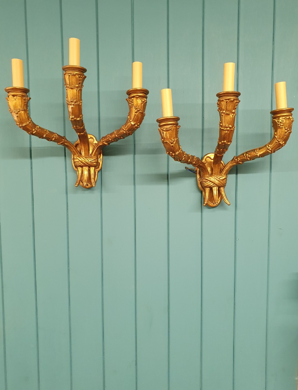 A pair of three-arm gilt metal French wall sconces designed to resemble tied organic branches, fitted with cream candle-drip sleeves.