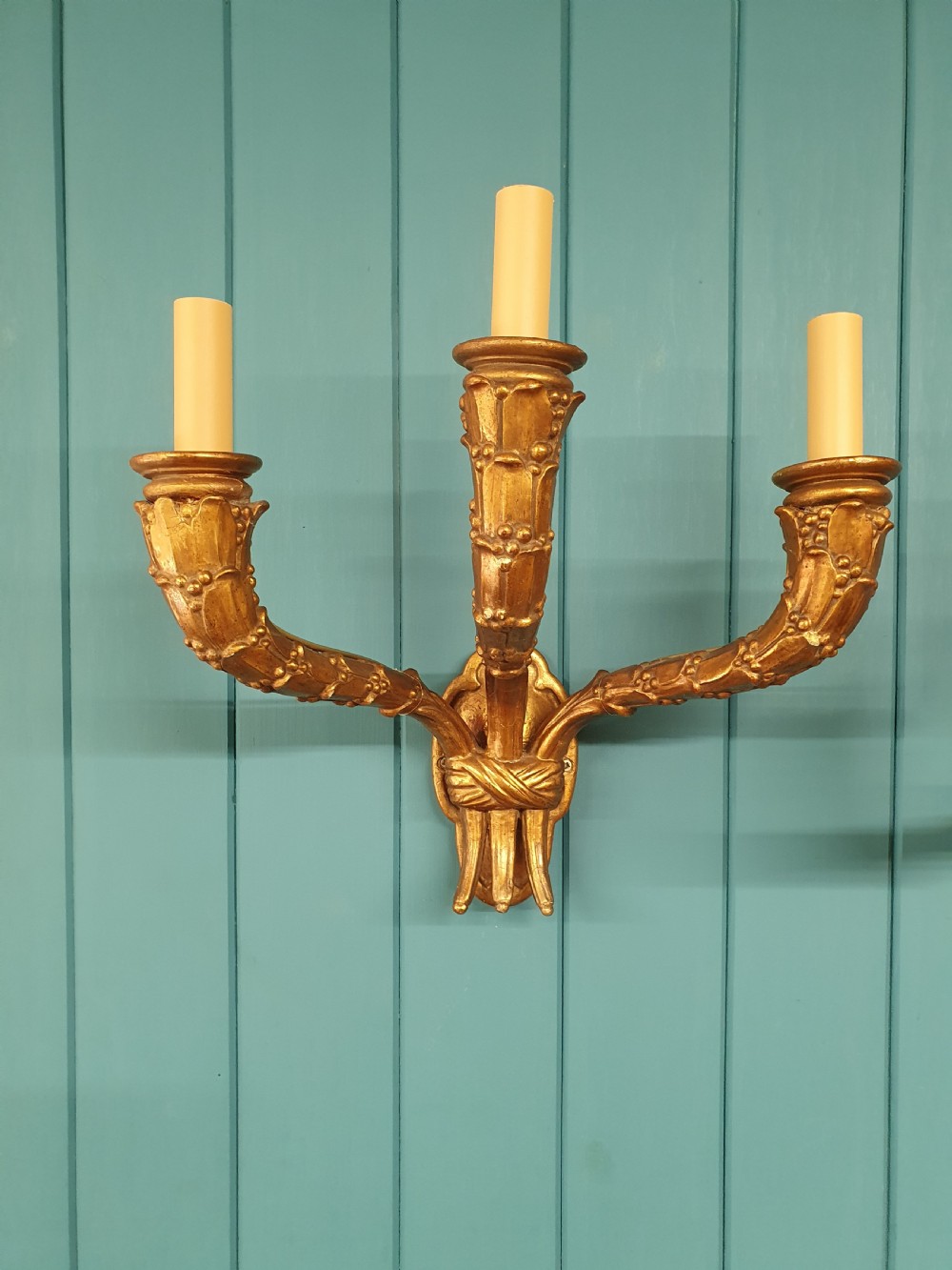 A pair of three-arm gilt metal French wall sconces designed to resemble tied organic branches, fitted with cream candle-drip sleeves. View V