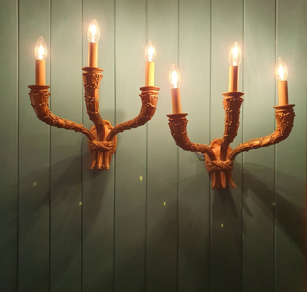 A pair of three-arm gilt metal French wall sconces designed to resemble tied organic branches, fitted with cream candle-drip sleeves. View VI