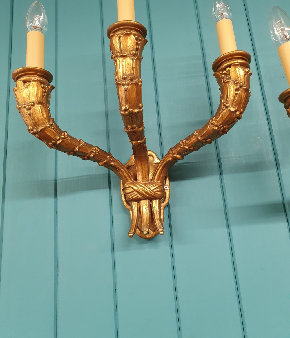 A pair of three-arm gilt metal French wall sconces designed to resemble tied organic branches, fitted with cream candle-drip sleeves. View VII