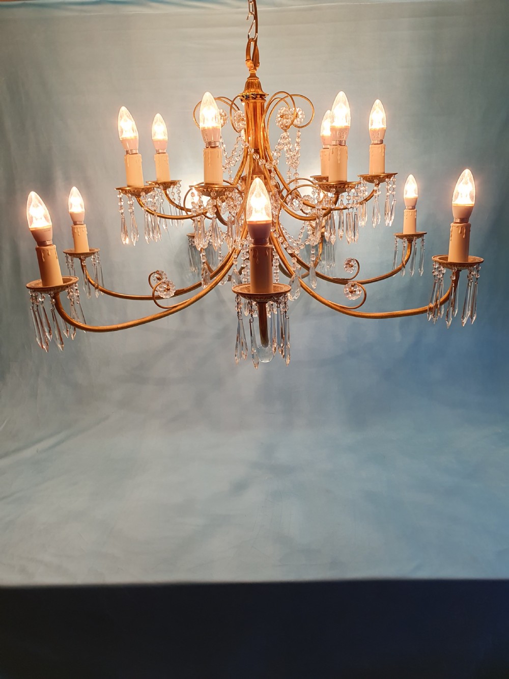 A pair of early 20th-century brass two-tier chandeliers decorated with cut glass crystal prisms, bead garlands, and candle sleeves. View IX