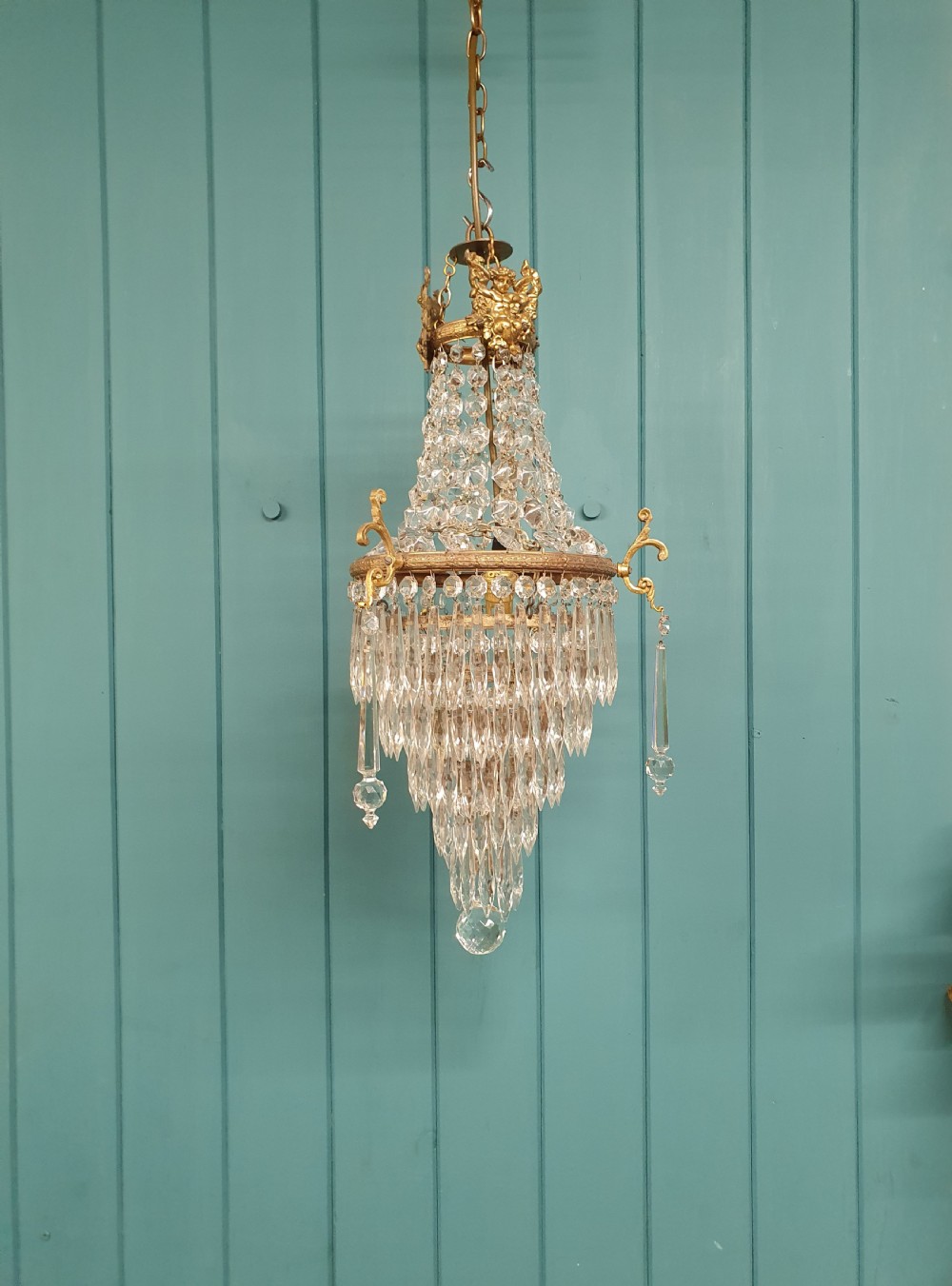 An early 20th-century cast brass chandelier with cherub gallery detailing and cascading crystal bead strands terminating in elongated glass spike prisms.