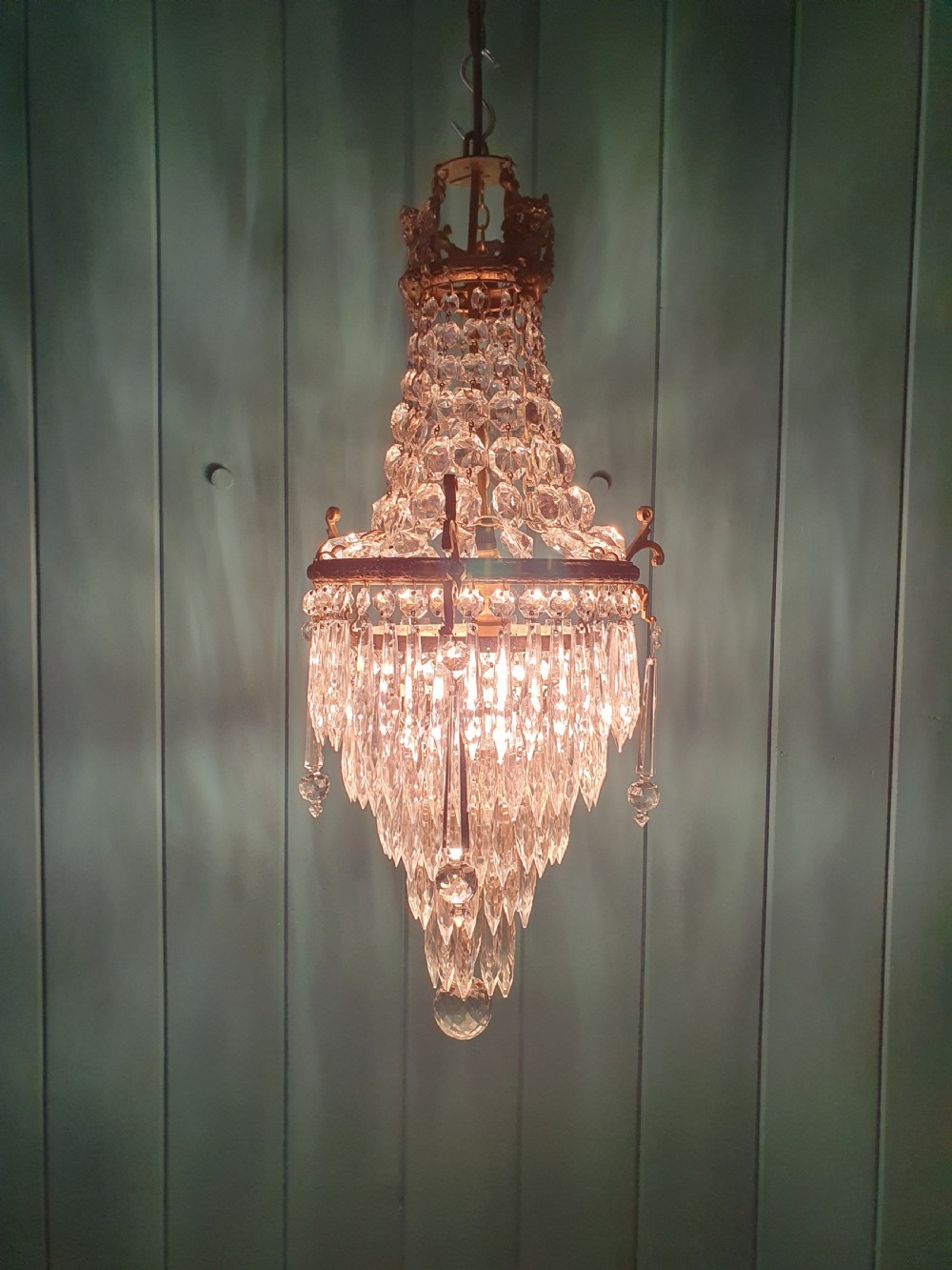 An early 20th-century cast brass chandelier with cherub gallery detailing and cascading crystal bead strands terminating in elongated glass spike prisms. View II