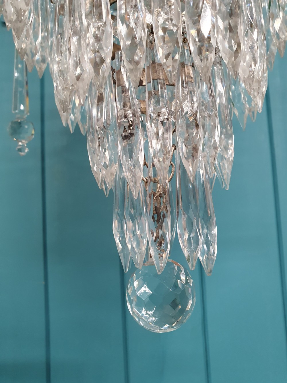 An early 20th-century cast brass chandelier with cherub gallery detailing and cascading crystal bead strands terminating in elongated glass spike prisms. View III