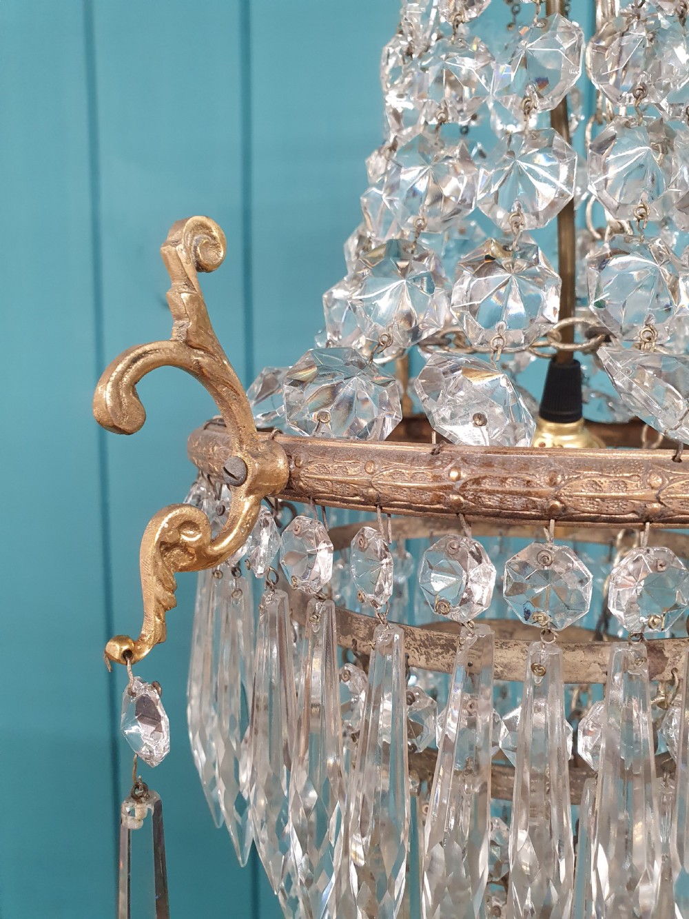 An early 20th-century cast brass chandelier with cherub gallery detailing and cascading crystal bead strands terminating in elongated glass spike prisms. View V