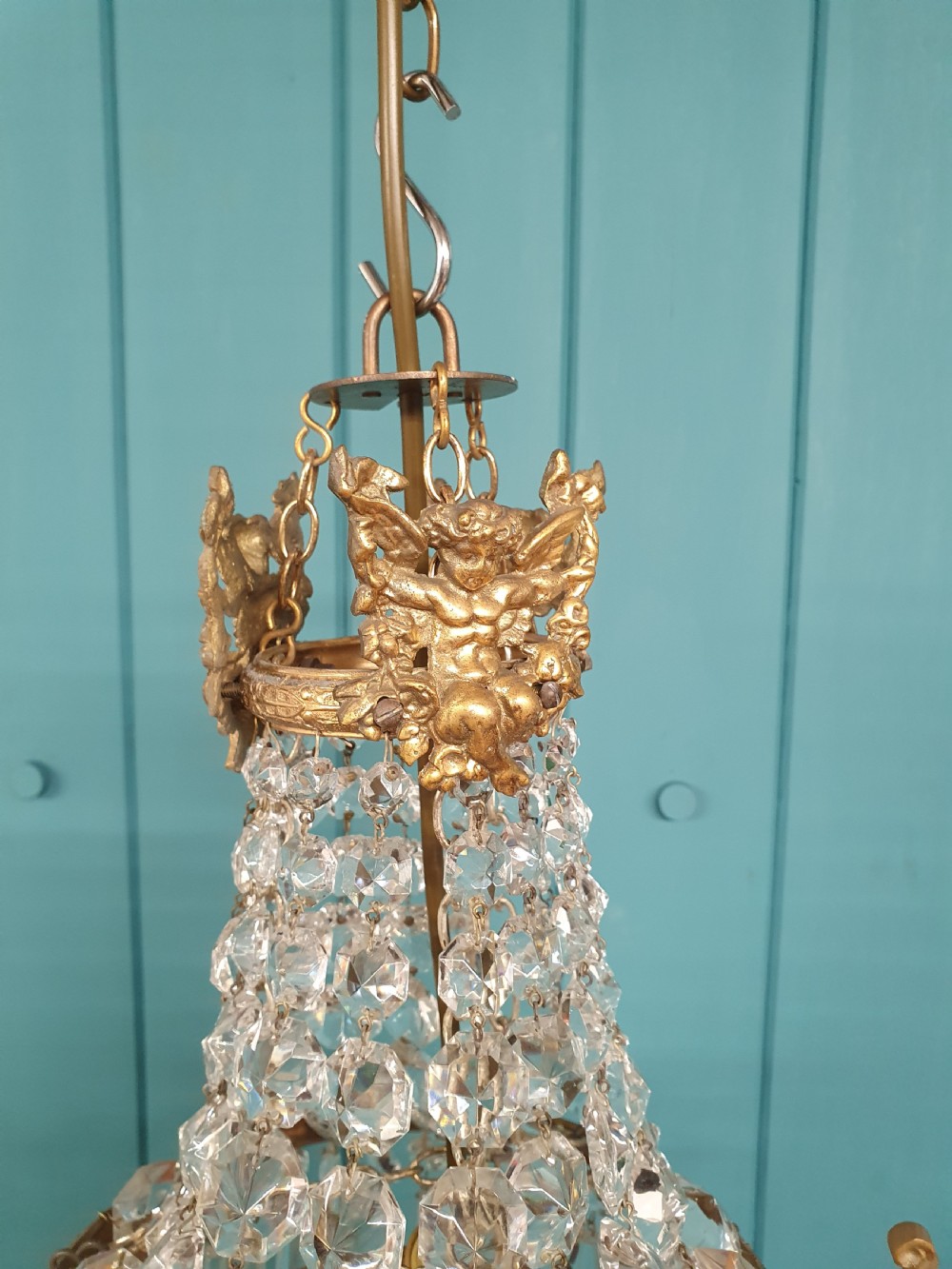 An early 20th-century cast brass chandelier with cherub gallery detailing and cascading crystal bead strands terminating in elongated glass spike prisms. View VI