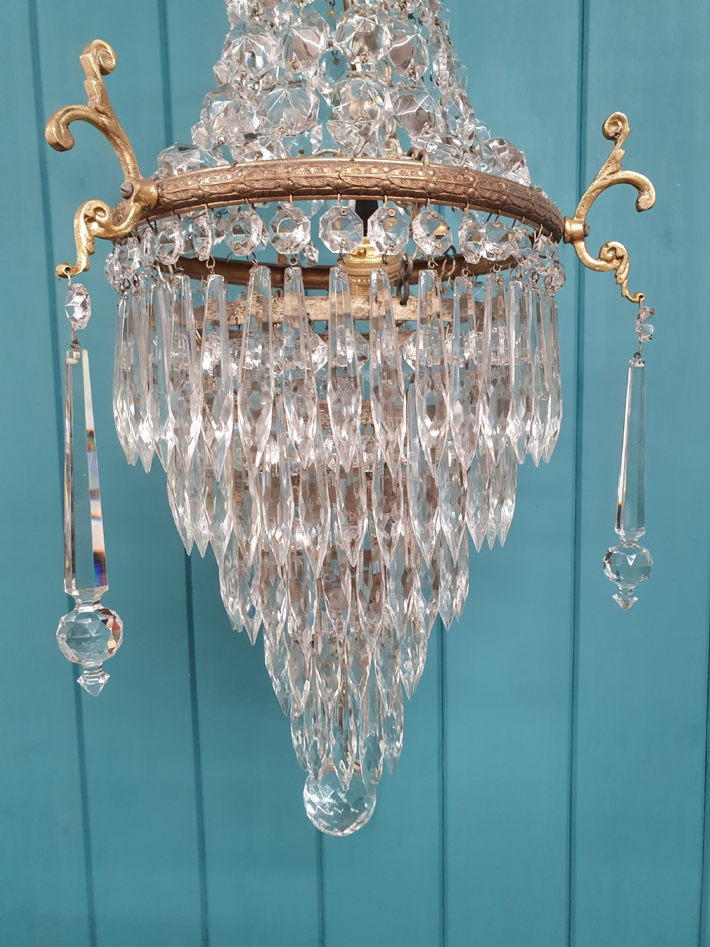 An early 20th-century cast brass chandelier with cherub gallery detailing and cascading crystal bead strands terminating in elongated glass spike prisms. View VII