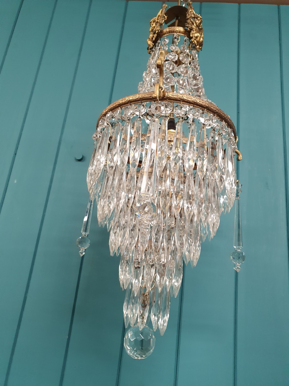 An early 20th-century cast brass chandelier with cherub gallery detailing and cascading crystal bead strands terminating in elongated glass spike prisms. View VIII