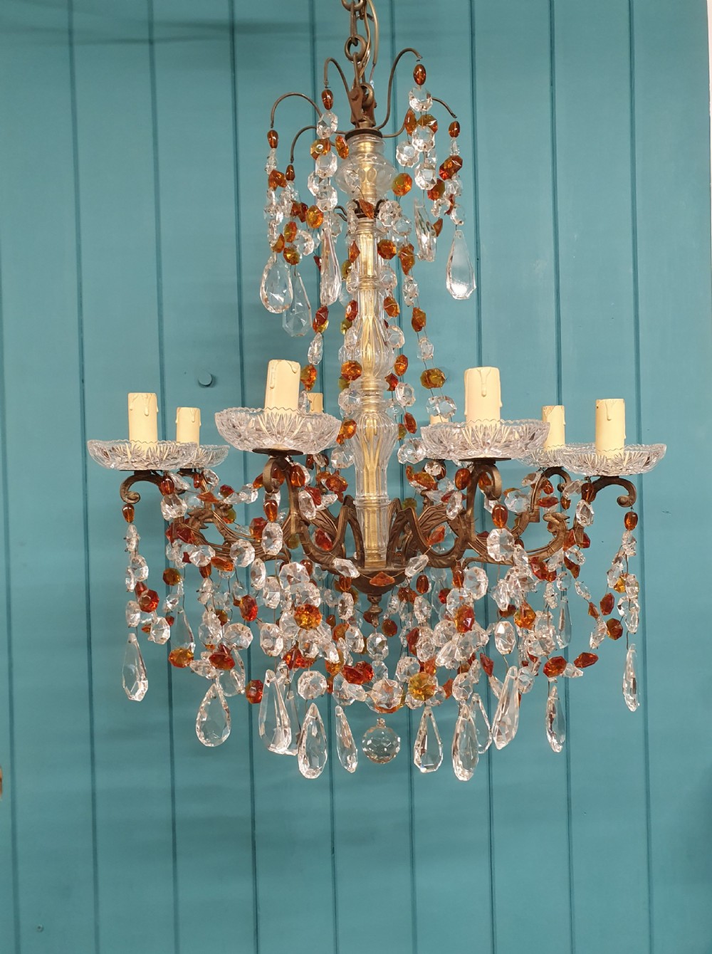 An early 20th century French brass chandelier featuring clear cut crystal droplets, amber glass beads, and candle-sleeve light fittings.