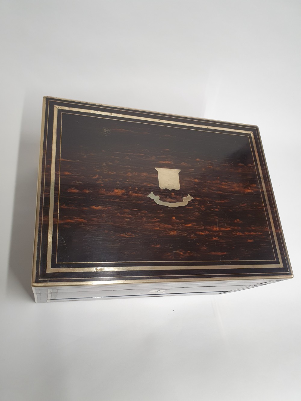 A Victorian dark brown coromandel wood dressing box with fine brass stringing, brass edging, and a central brass shield cartouche. View II