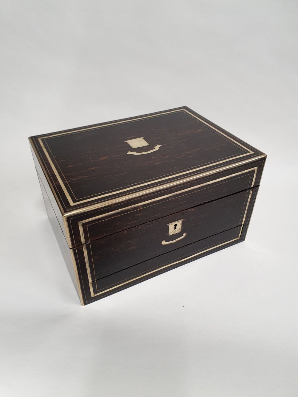 A Victorian dark brown coromandel wood dressing box with fine brass stringing, brass edging, and a central brass shield cartouche.