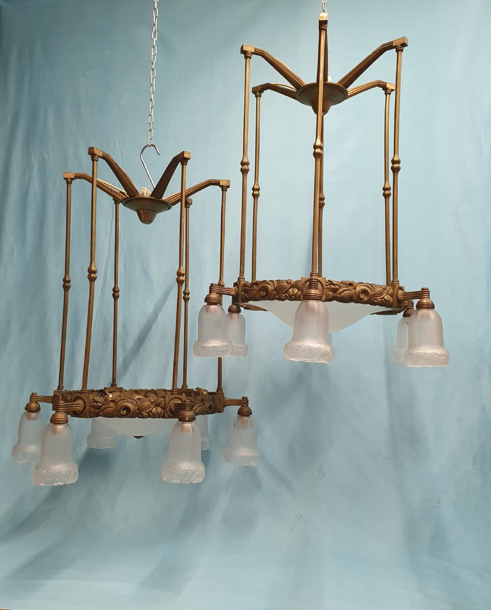 A pair of early 20th-century brass pendant lights featuring tall angular cage frames supporting ornate floral band bases with multiple suspended frosted glass shades.