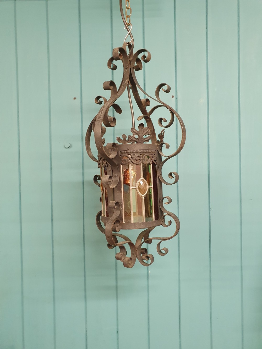 An early 20th-century hanging French porch lantern crafted from dark wrought iron scrollwork with leaded glass panels.