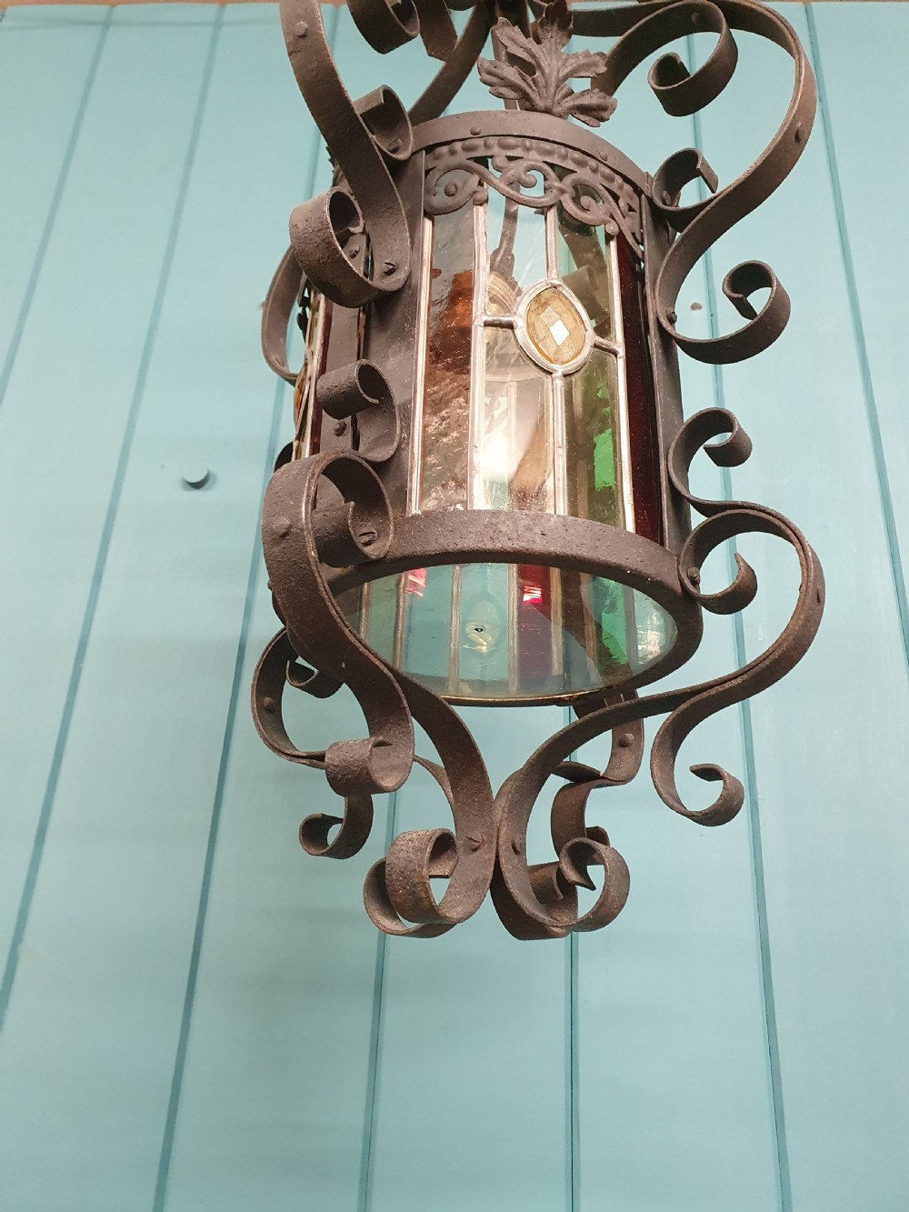 An early 20th-century hanging French porch lantern crafted from dark wrought iron scrollwork with leaded glass panels. View II