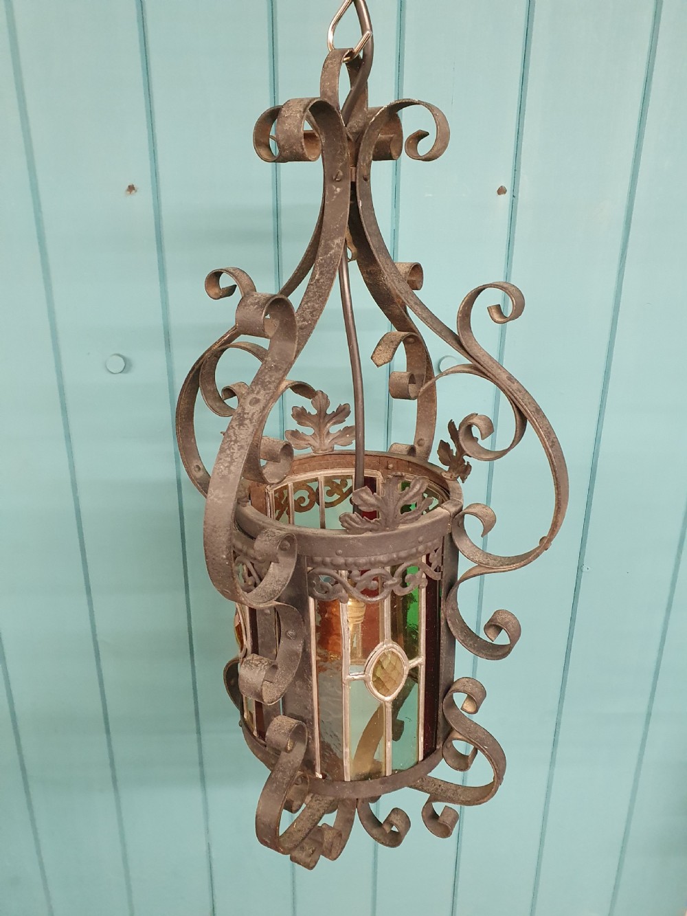 An early 20th-century hanging French porch lantern crafted from dark wrought iron scrollwork with leaded glass panels. View VI