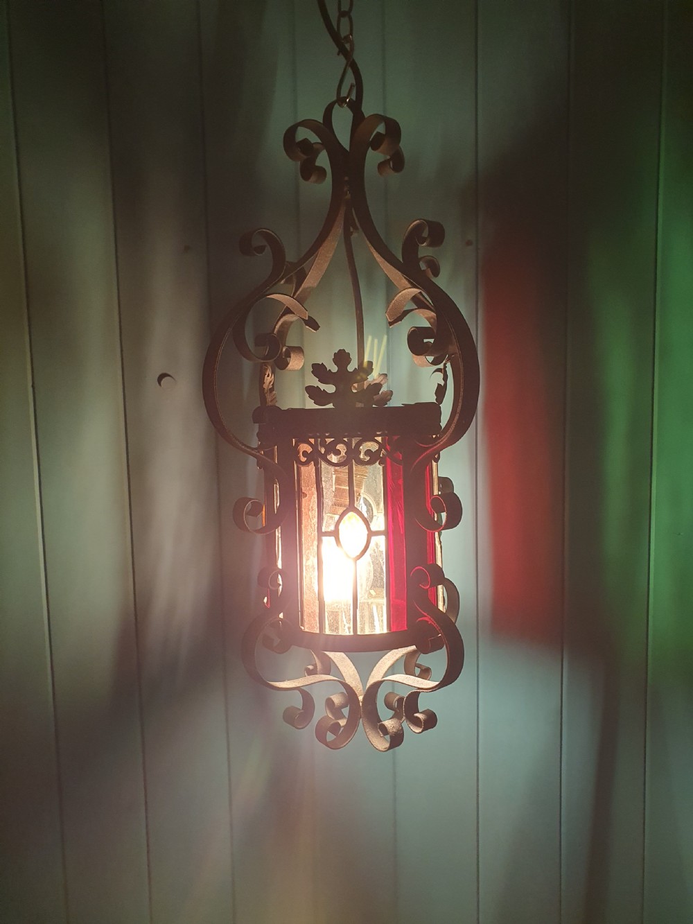 An early 20th-century hanging French porch lantern crafted from dark wrought iron scrollwork with leaded glass panels. View VII