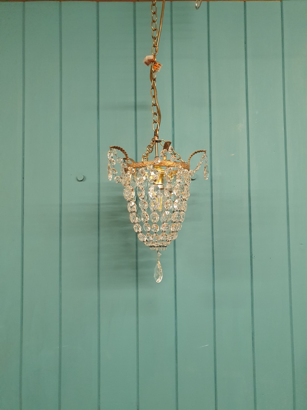 A small early 20th-century ceiling pendant featuring a brass frame hung with faceted clear glass crystal beads formed into a tapered basket shape.