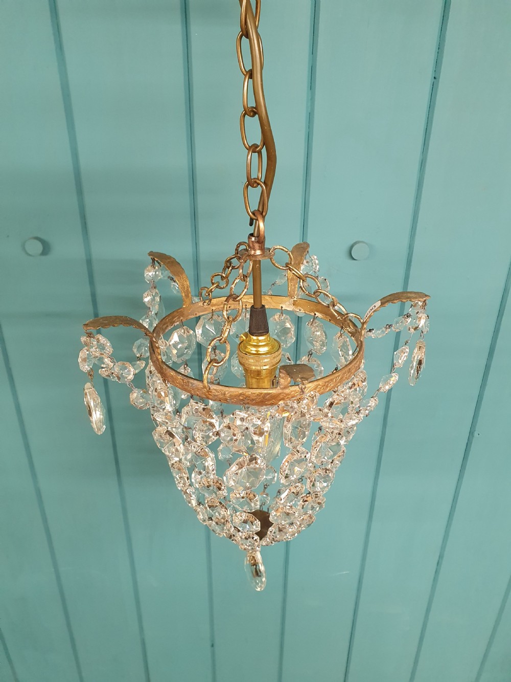 A small early 20th-century ceiling pendant featuring a brass frame hung with faceted clear glass crystal beads formed into a tapered basket shape. View V