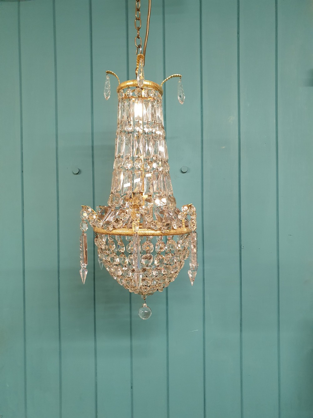 An early 20th-century swag chandelier with tiered glass crystal prisms and a gilt brass frame hanging from a chain.