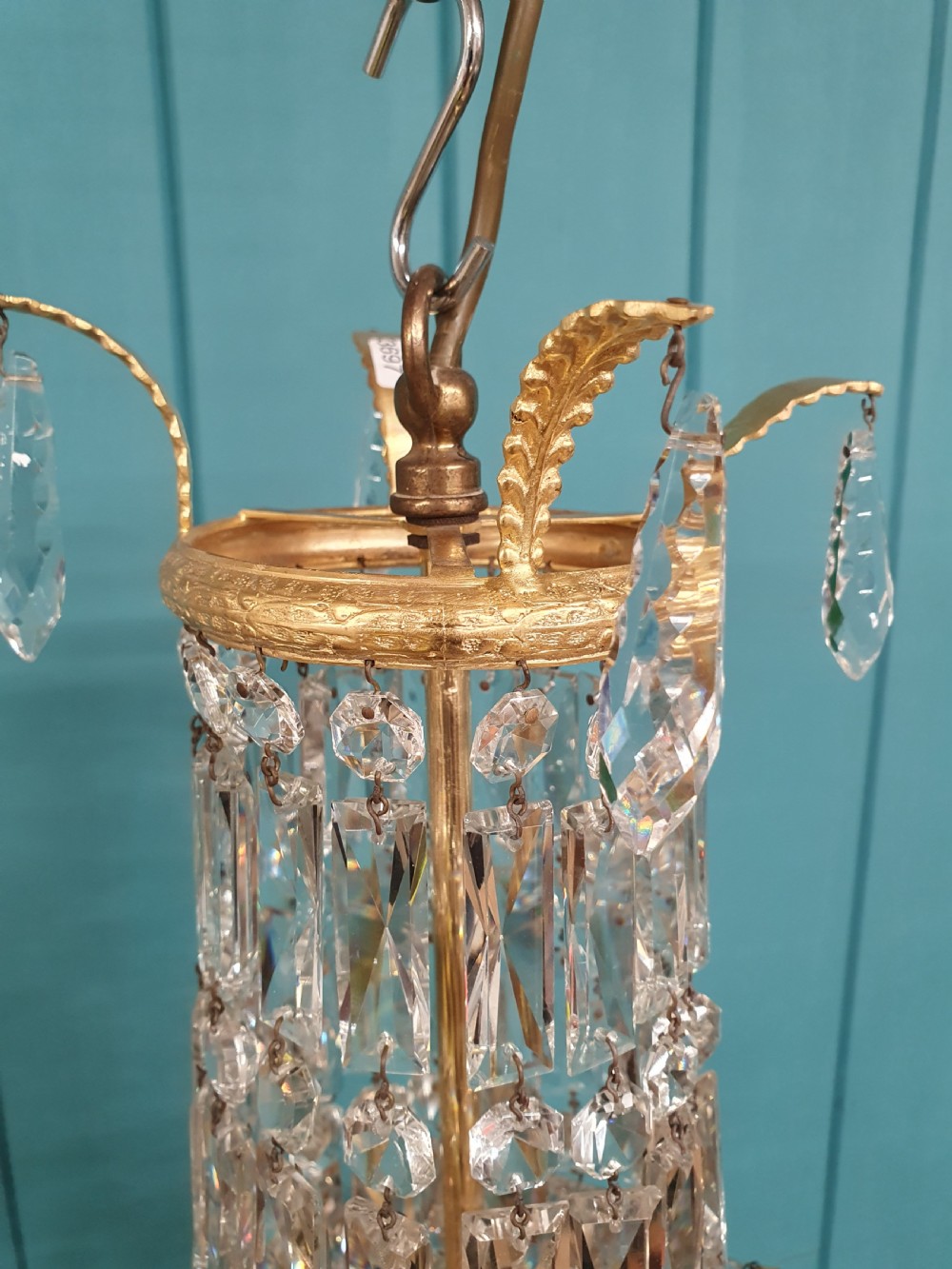 An early 20th-century swag chandelier with tiered glass crystal prisms and a gilt brass frame hanging from a chain. View II