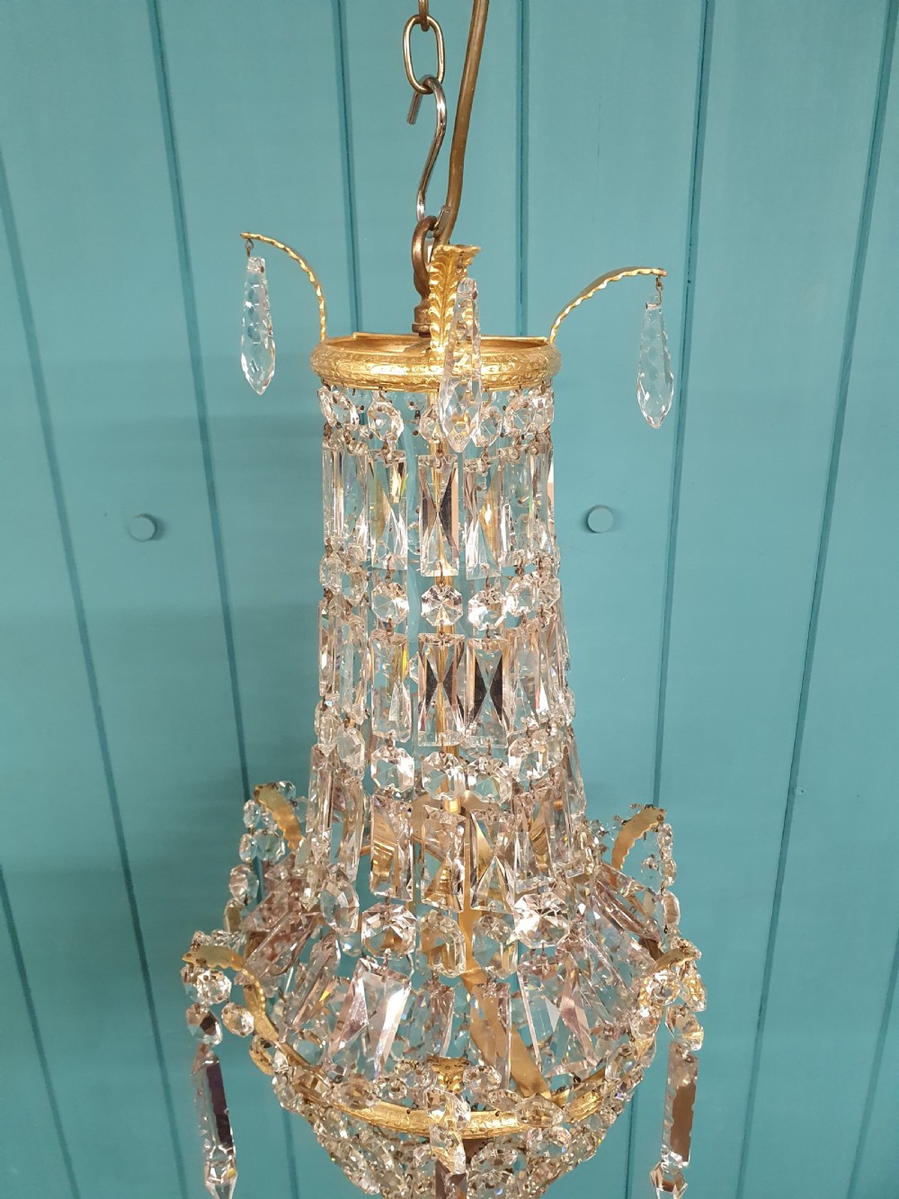 An early 20th-century swag chandelier with tiered glass crystal prisms and a gilt brass frame hanging from a chain. View V