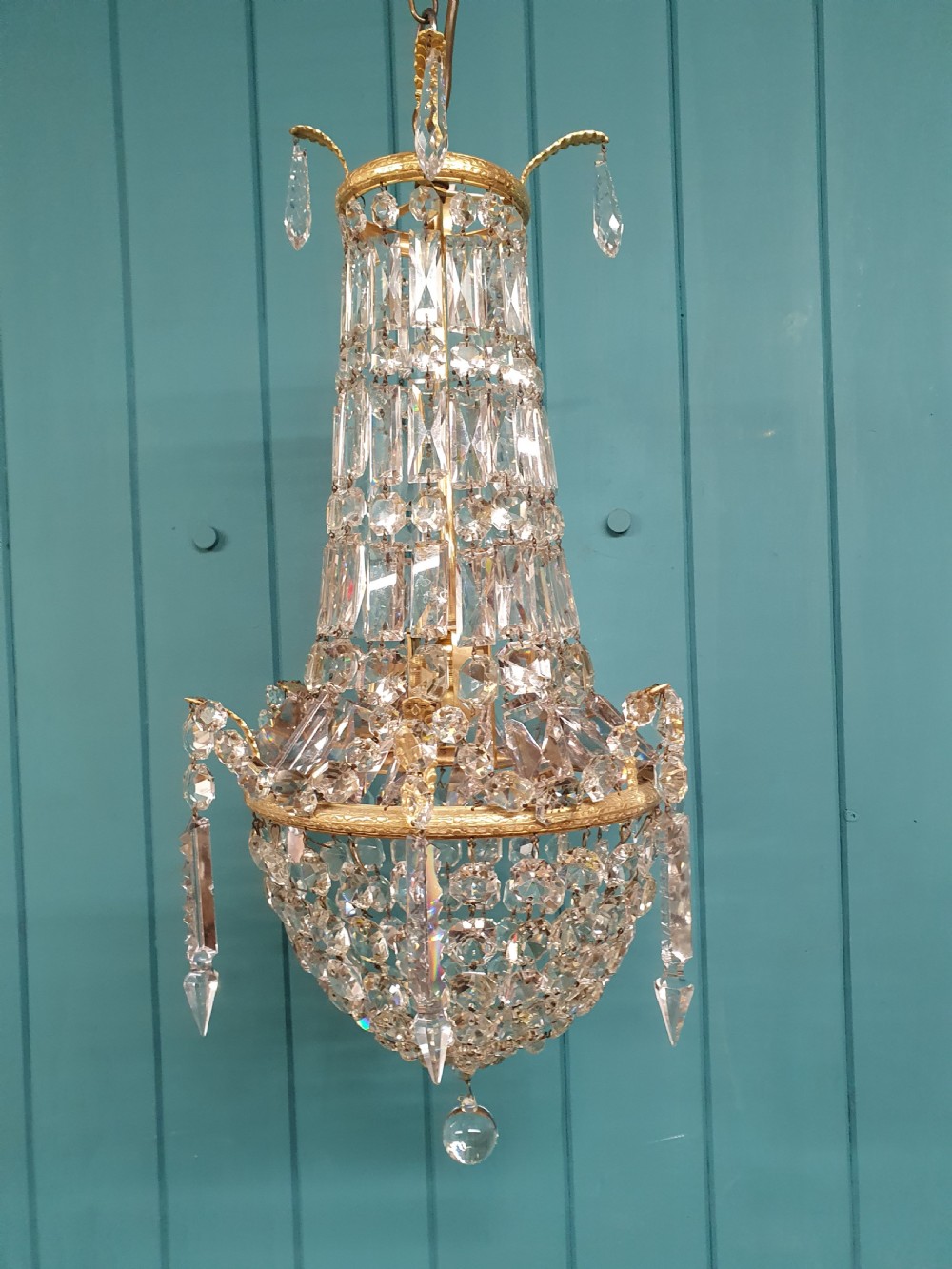 An early 20th-century swag chandelier with tiered glass crystal prisms and a gilt brass frame hanging from a chain. View VI