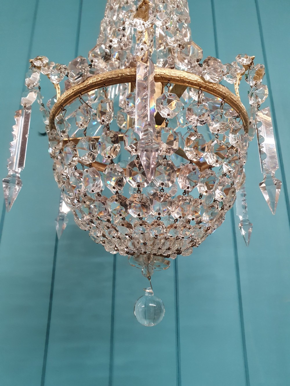 An early 20th-century swag chandelier with tiered glass crystal prisms and a gilt brass frame hanging from a chain. View VII