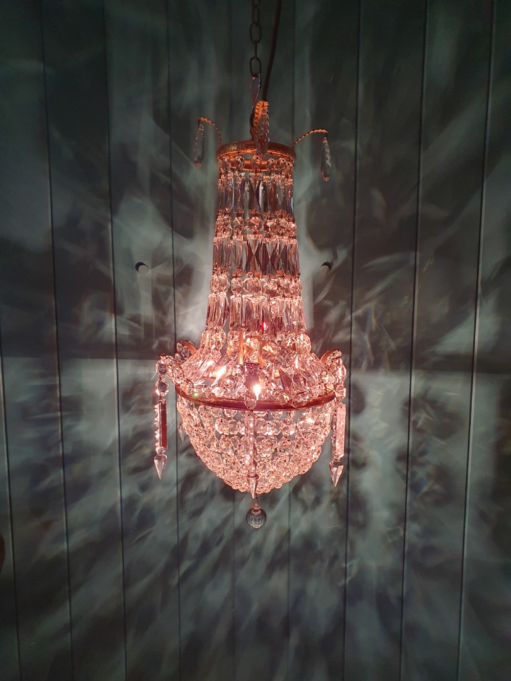 An early 20th-century swag chandelier with tiered glass crystal prisms and a gilt brass frame hanging from a chain. View IX