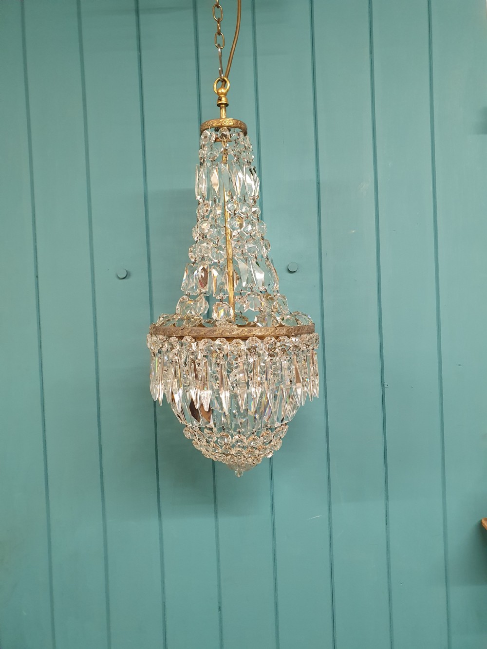 An early 20th-century crystal bag chandelier featuring cascading glass droplets suspended from a decorative brass gallery ring and chain.