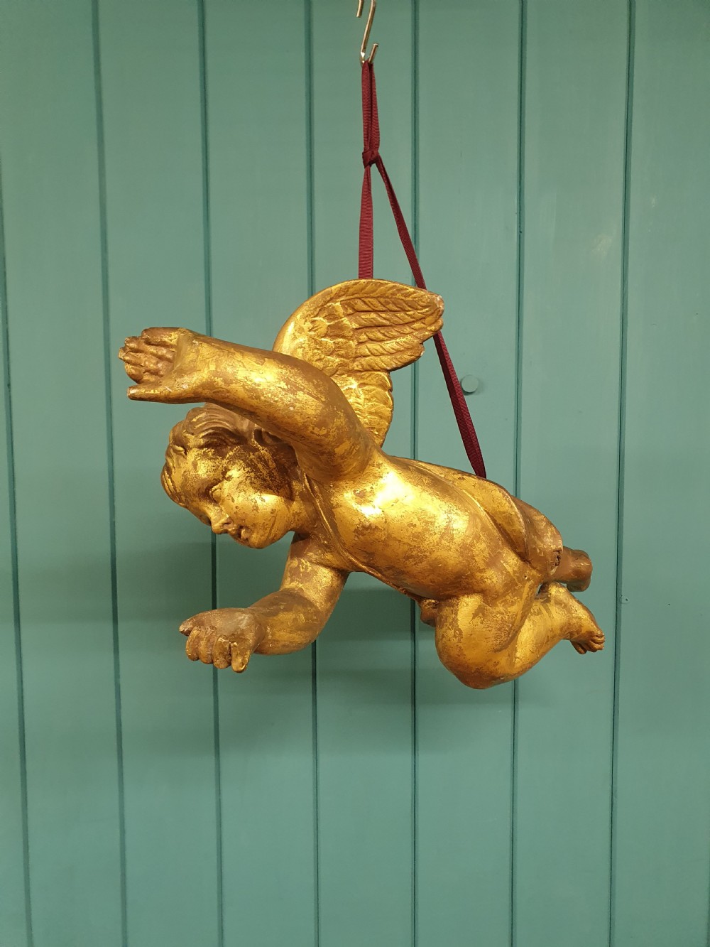 A late 19th-century hand-carved wooden cherub figure with feathered wings and extended limbs, finished in gold leaf gilding.