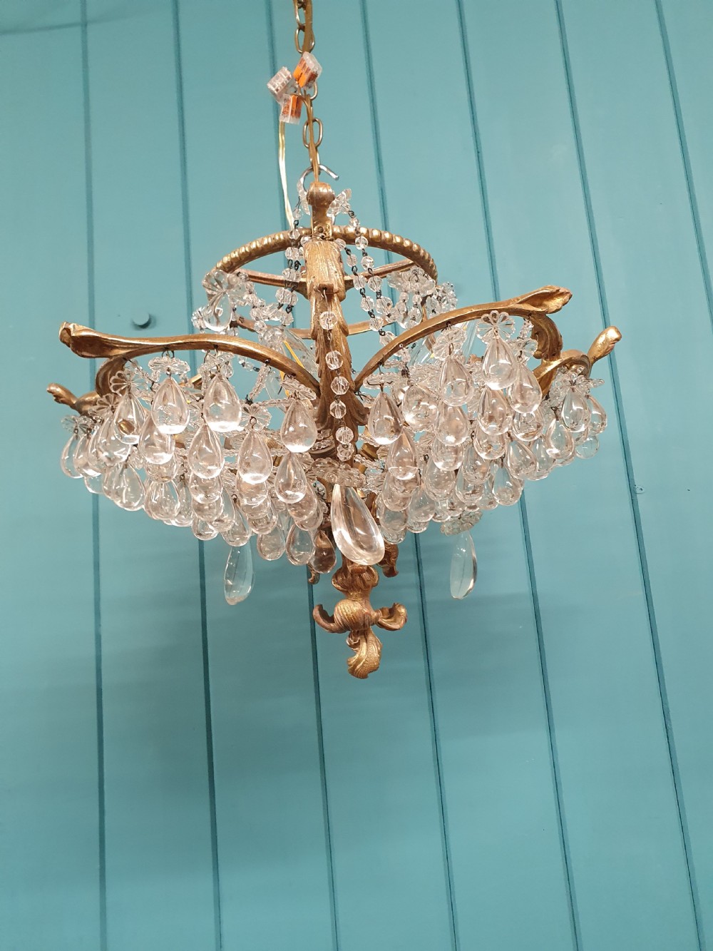 An early 20th-century gilded brass chandelier featuring sweeping leaf-form arms and cascading clear glass teardrop and grape-form droplets.