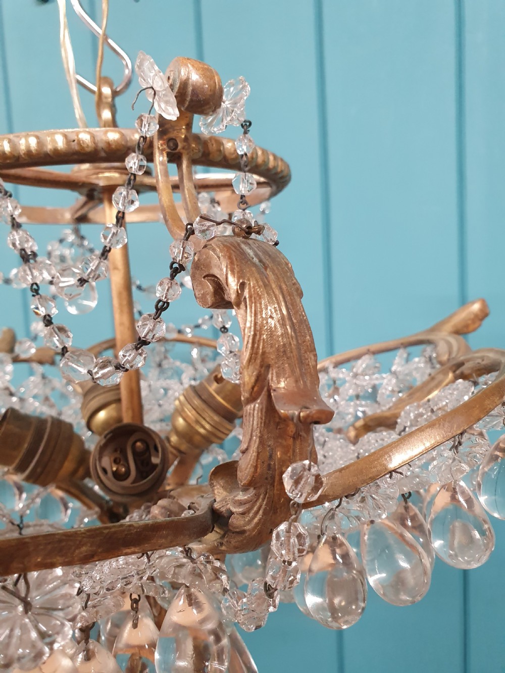 An early 20th-century gilded brass chandelier featuring sweeping leaf-form arms and cascading clear glass teardrop and grape-form droplets. View II