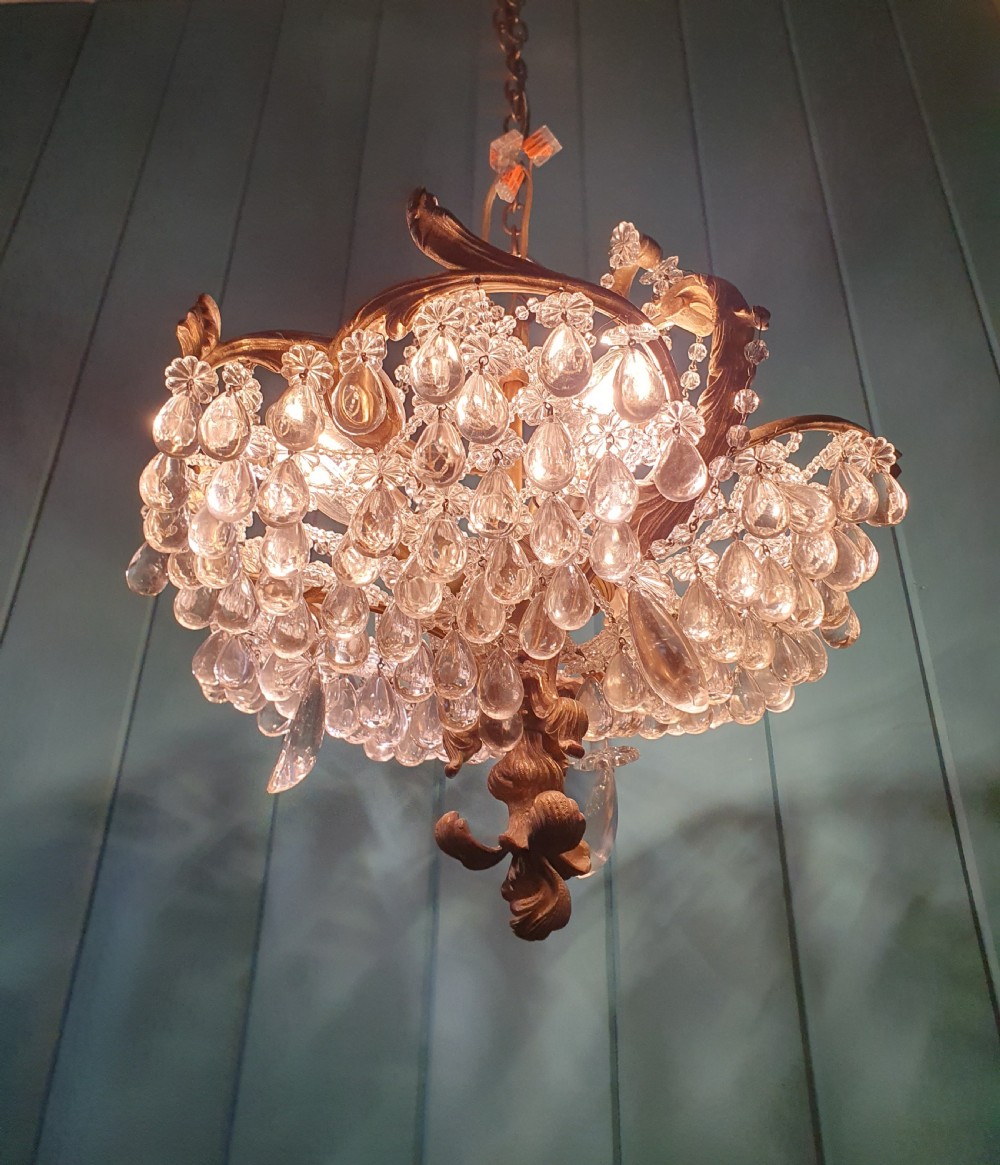 An early 20th-century gilded brass chandelier featuring sweeping leaf-form arms and cascading clear glass teardrop and grape-form droplets. View V