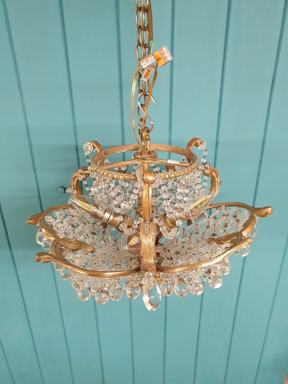 An early 20th-century gilded brass chandelier featuring sweeping leaf-form arms and cascading clear glass teardrop and grape-form droplets. View VI